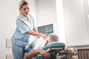 A chiropractor gently examining a young person's upper back and spine in a clinical setting.