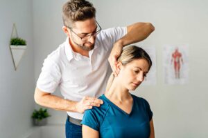 Adult gently stretching a sore lower back beside a chair in a bright home setting.