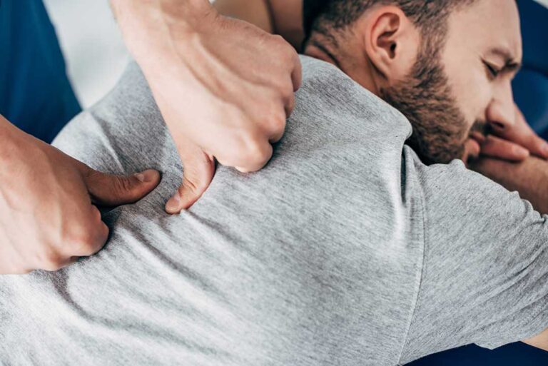 Clinician assessing a seated adult’s neck and shoulder movement in a bright treatment room.